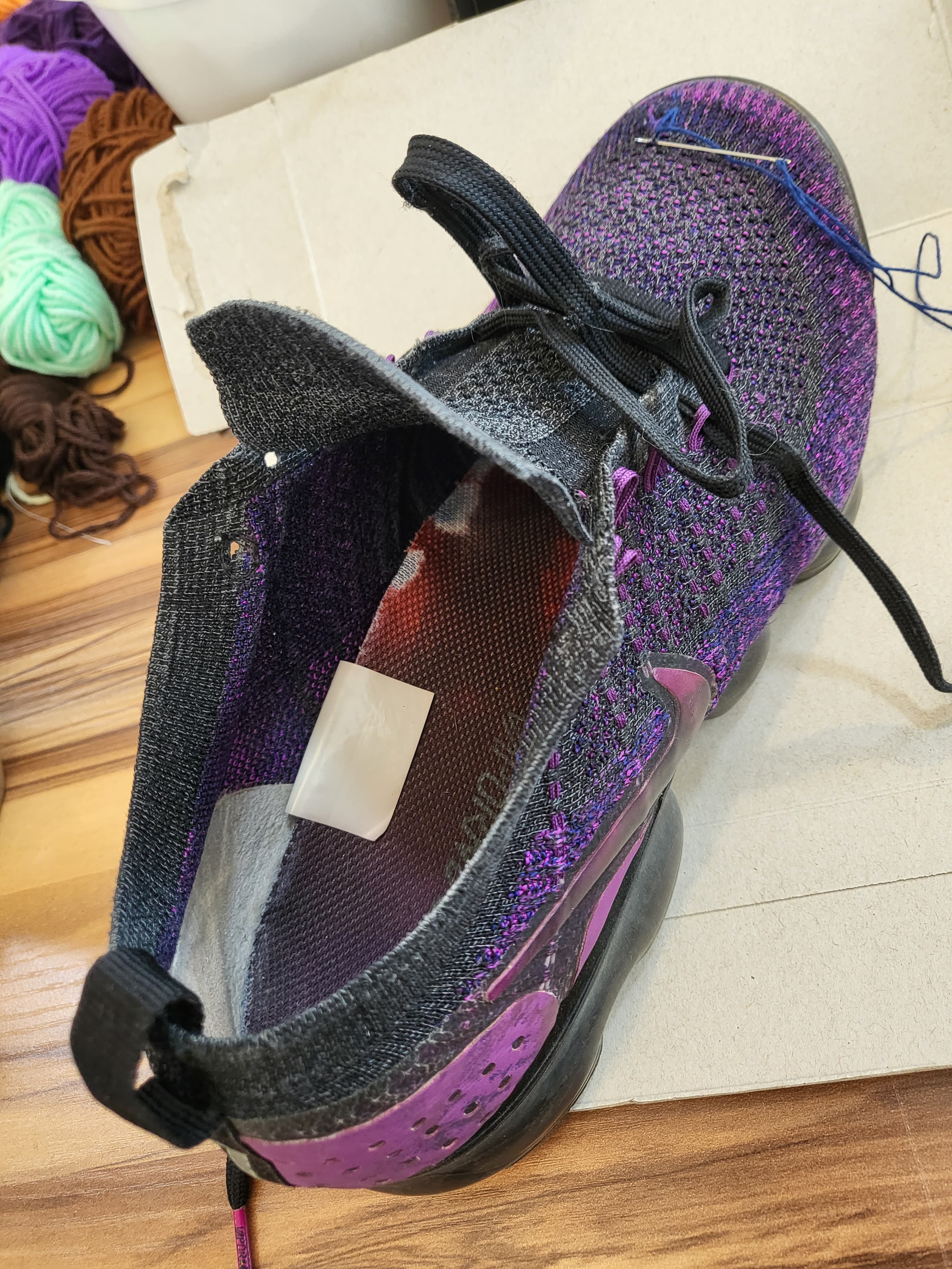 Vapormax on a darning mushroom, blue thread in progress — yarn balls blurred in the background