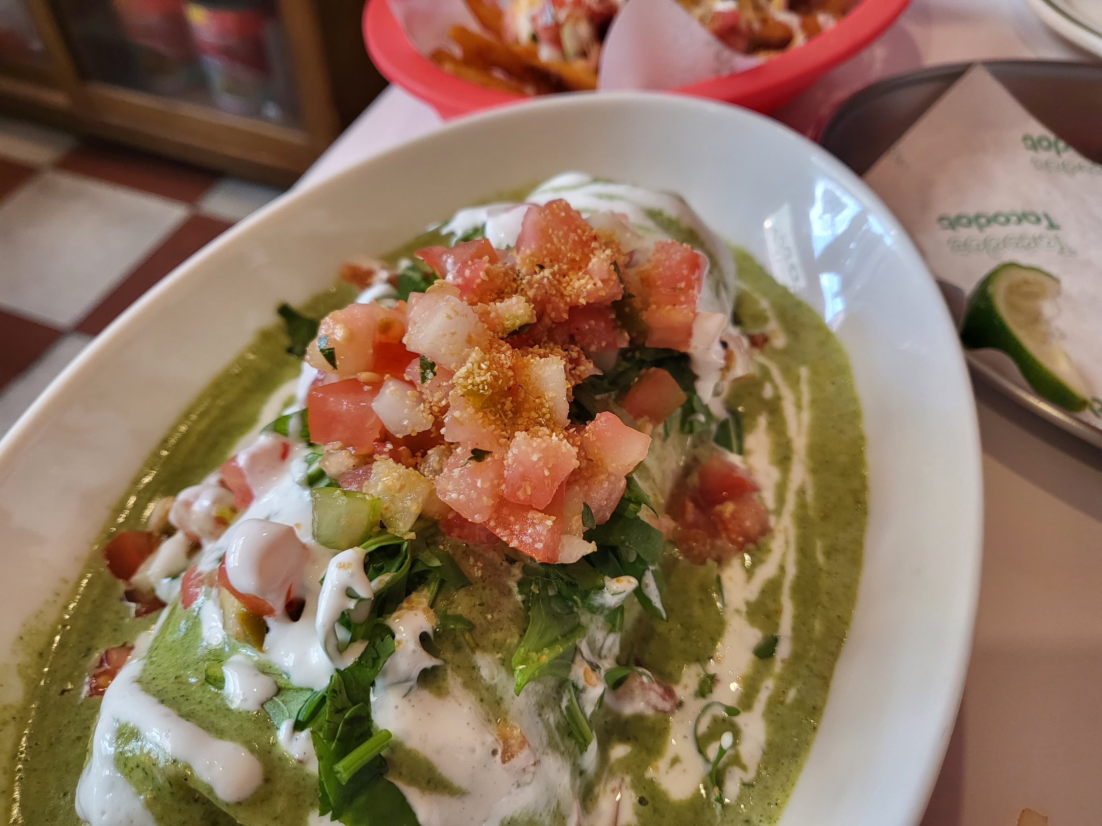 Tacodot verde sauce enchilada — green salsa on a white oval plate